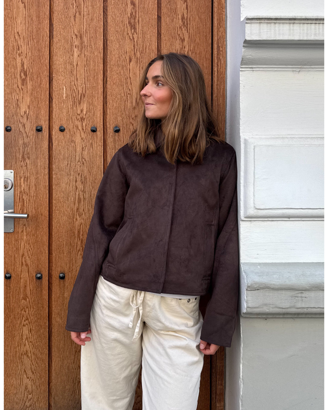 Modelfoto af pige i brun Allie ruskinds jakke og beigefarvede Arianna jeans. Alt er fra BySofieSønderby