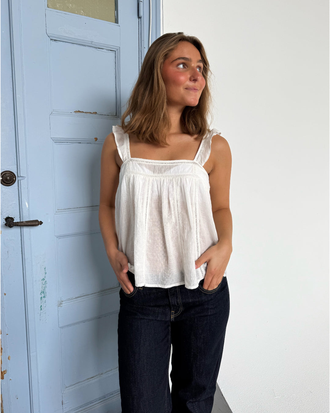 Modelfoto af pige som bærer en Amona top i hvid, samt et par mørkeblå jeans. Alt fra By Sofie Sønderby