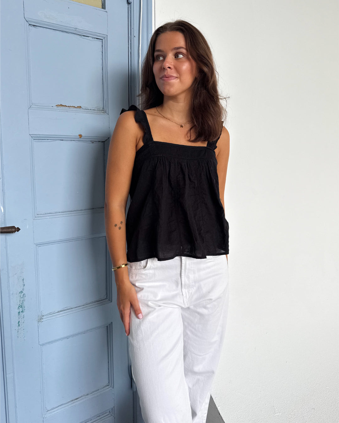Modelfoto af pige som bærer en Amona top i sort, samt et par mørkeblå jeans. Alt fra By Sofie Sønderby