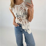 En person iført en hvid, detaljeret hæklet top tager en selfie med en smartphone. Personen har også lyseblå jeans på og står i et minimalistisk rum med lyse vægge.