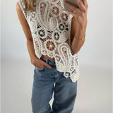 En person iført en hvid, mønstret, hæklet top tager et spejl-selfie og har en hånd i lommen på et par blå jeans i et neutralt indendørsmiljø.