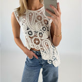 En kvinde iført en hvid, mønstret, ærmeløs top tager et selfie med en smartphone. Hun står i lyseblå jeans i et minimalistisk rum.