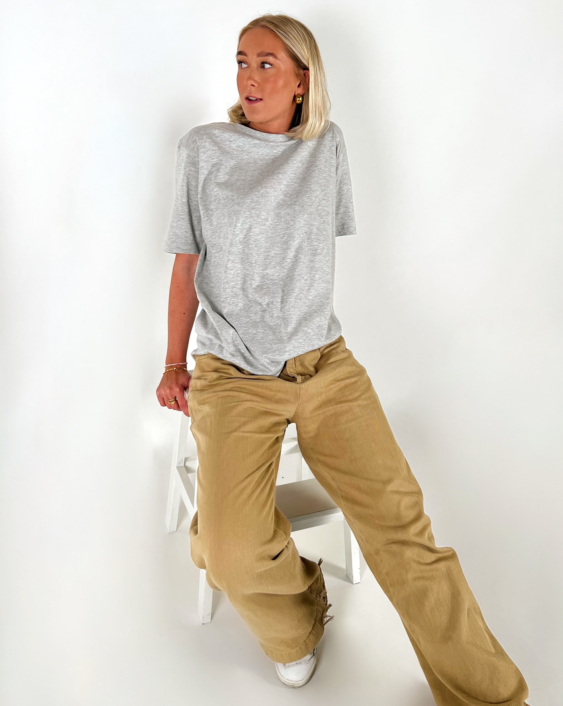 Person sidder på en hvid stol iført grå T-shirt og beige bukser. Personen ser til siden i et neutralt, hvidt rum.
