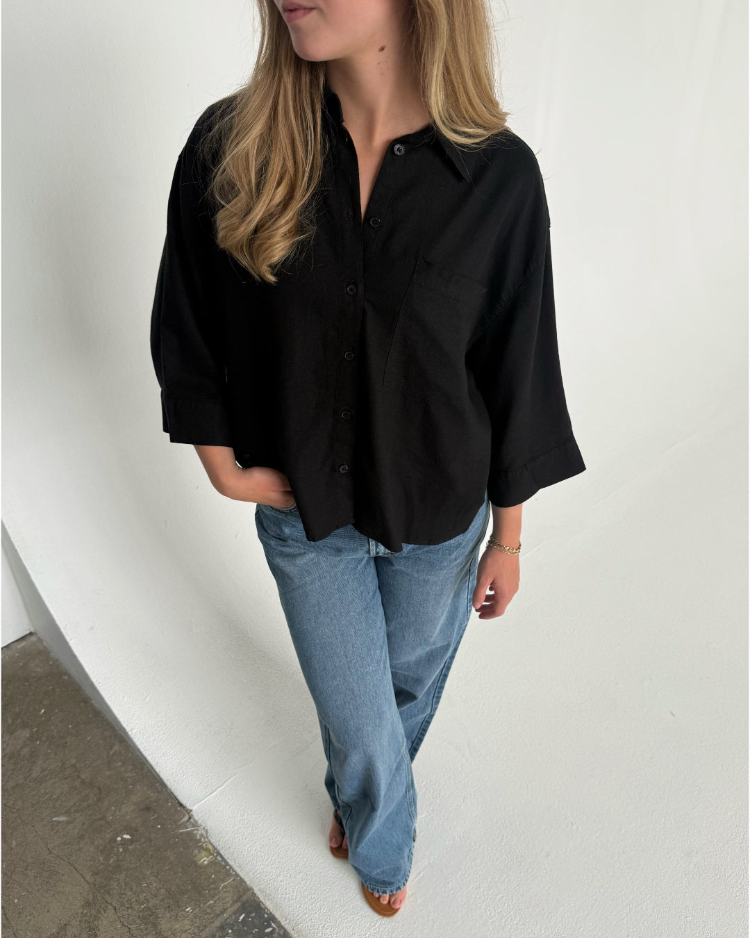 Modelfoto af pige som bærer en Breeze skjorte i sort, samt et par blå Nanna jeans og Carmen sandaler. Alt fra By Sofie Sønderby