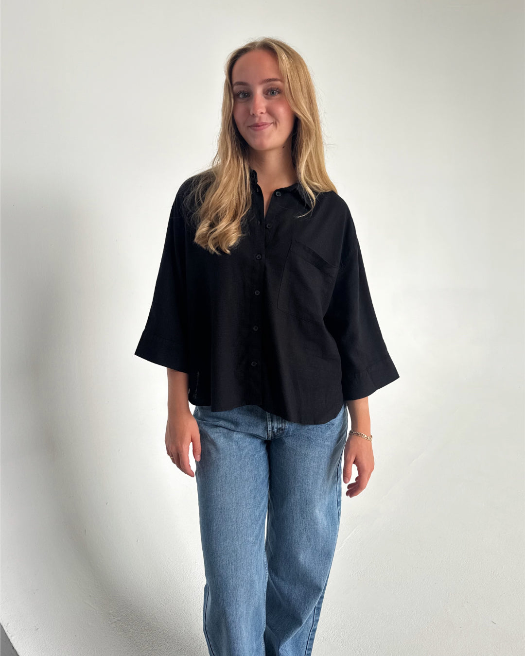 Modelfoto af pige som bærer en Breeze skjorte i sort, samt et par blå Nanna jeans. Alt fra By Sofie Sønderby
