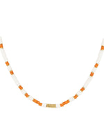 Halskæde af perler, vekslende mellem hvide og orange farver, med en lille guld detalje i midten. Ligger mod en simpel hvid baggrund.