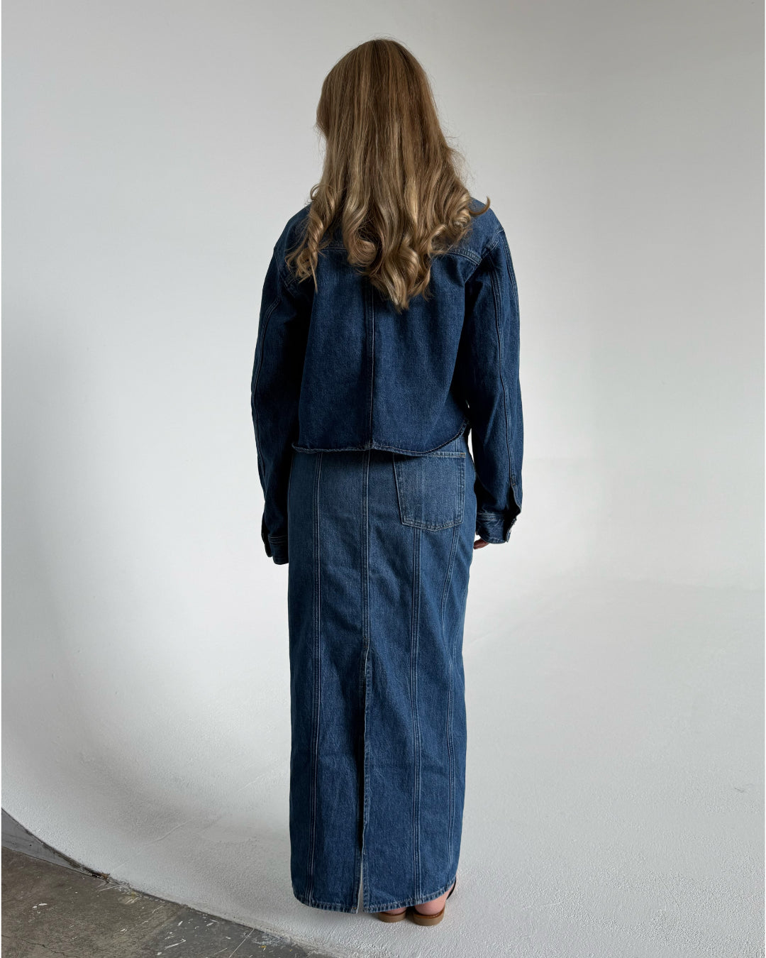 Modelfoto af pige som bærer en blå Cana denim nederdel, samt Cana denim jakke og sorte Carmen sandaler. Alt fra By Sofie Sønderby