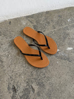 Et par brune flip-flops ligger stille på en grå, rå betonoverflade i et sparsomt belyst rum.