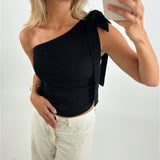 Person tager selfie iført sort, skulderfri top og lyse bukser, med mobilen i hånden. De står i et lyst rum, og telefonens mærke "CASEYNI" er synligt.