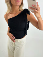 Person tager selfie iført sort, skulderfri top og lyse bukser, med mobilen i hånden. De står i et lyst rum, og telefonens mærke "CASEYNI" er synligt.