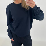 En person iført sort sweatshirt tager et spejlfoto med en smartphone i en lys, minimalistisk baggrund.