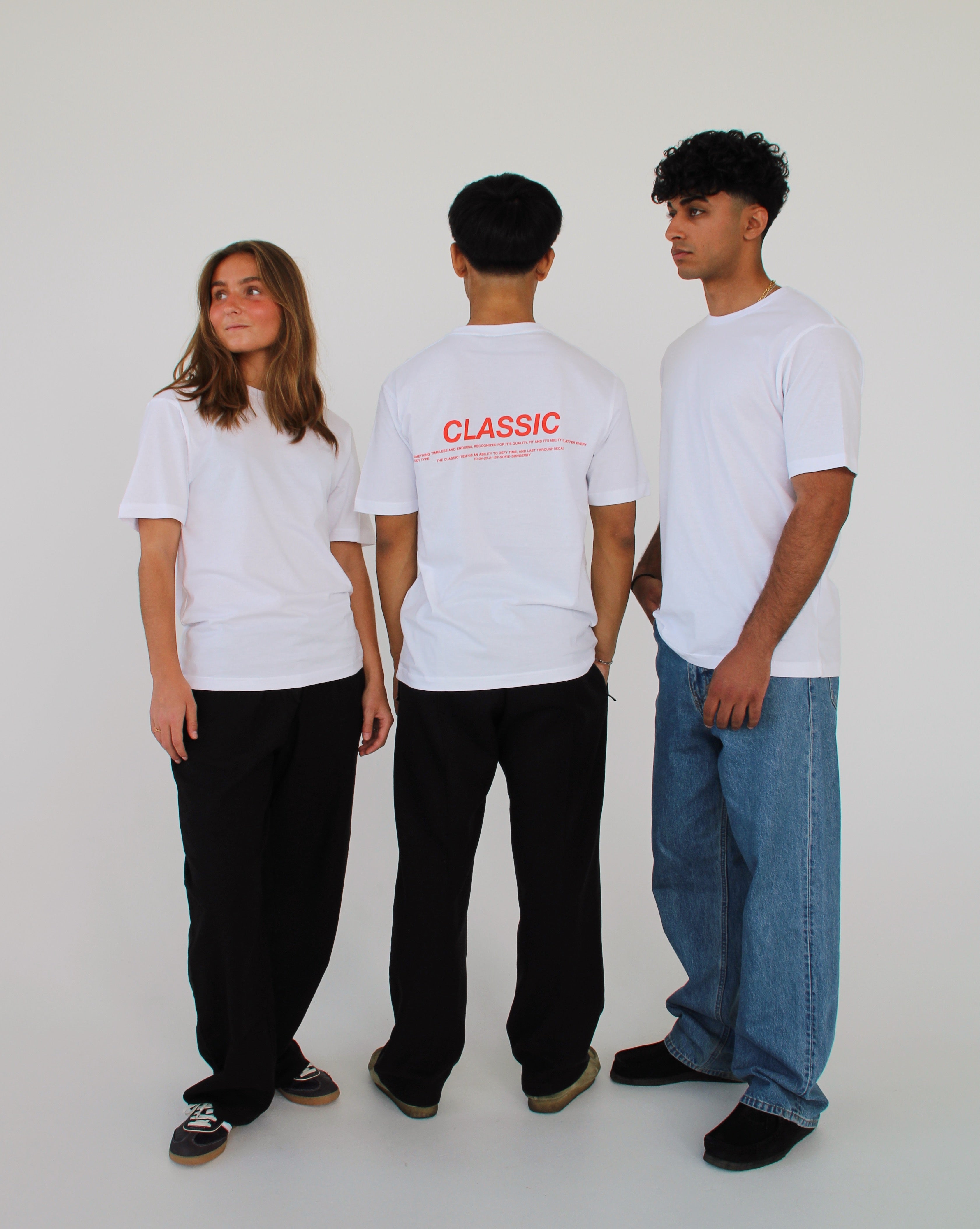 Tre personer iført hvide t-shirts står i hvidt rum. En person viser ryggen med teksten "CLASSIC" i rød på t-shirten. De andre ser forskellige retninger.