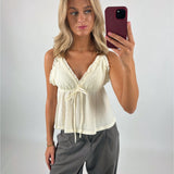 En person tager en selfie iført en lyseblå top og grå bukser. Personen står i et rum med en lys baggrund og holder en rød mobiltelefon.