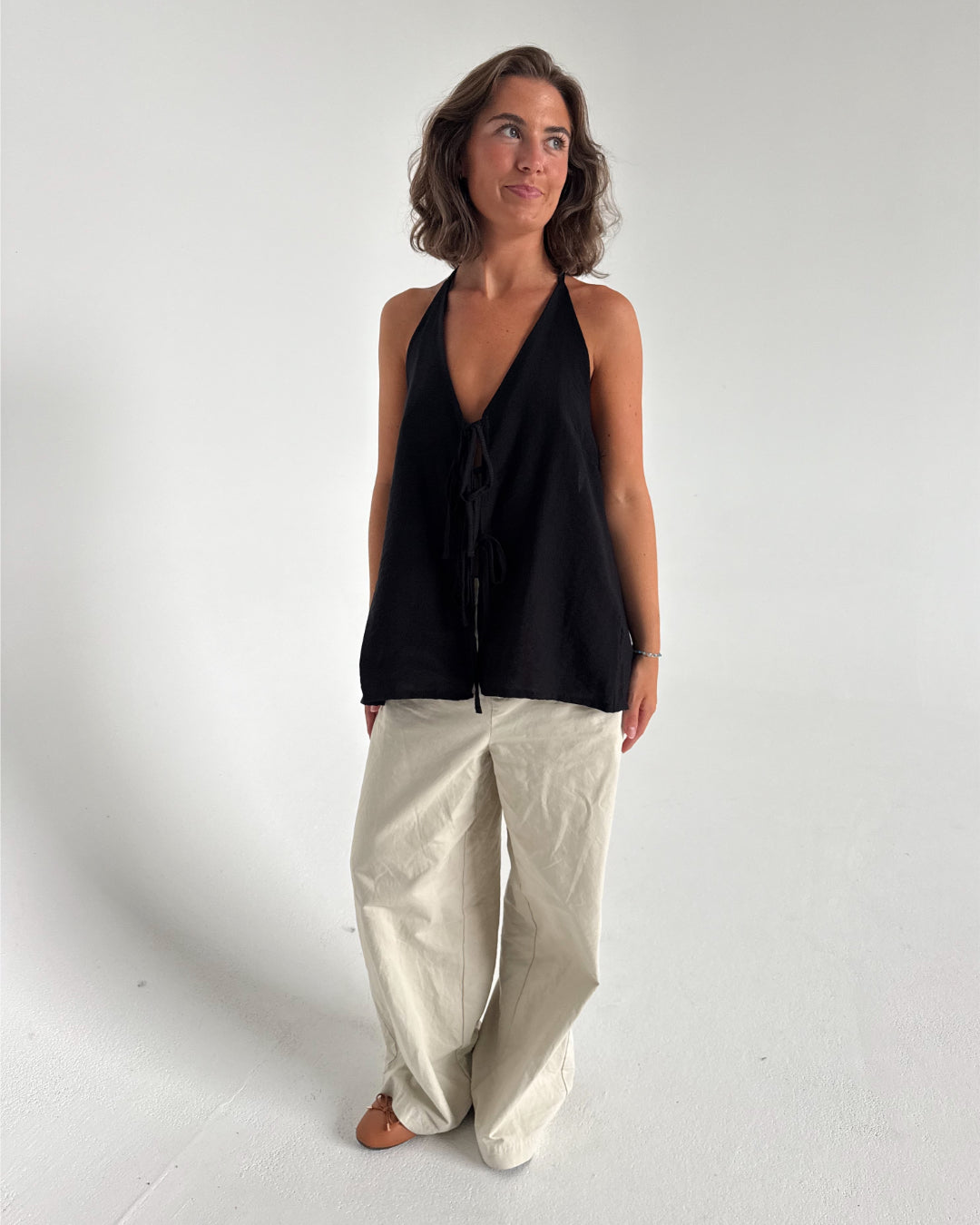 Modelfoto af pige som bærer en Daisy top i sort, samt et par beige Yale bukser. Alt fra By Sofie Sønderby