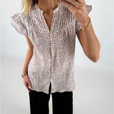 En person iført en blomstret skjorte tager et spejlbillede med en smartphone. Personen bærer også sorte bukser og et armbånd, og står i et lyst rum.