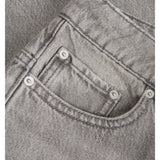 Grå jeanslomme med synlige sømme og metalknapper, placeret mod en baggrund af denimstof i samme farve og tekstur.