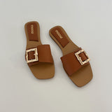 To brune sandaler med store, firkantede spænder ligger på en flad, hvid overflade. Mærket "moow" er trykt indeni sålerne.