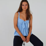 En person sidder på en barstol og kigger fremad. Personen bærer en blå top og mørke bukser i et enkelt studie med en hvid baggrund.