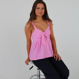 En person sidder stille på en hvid, metal-stol, iført en lyserød top og sorte bukser, med hvid baggrund.