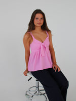 En person sidder stille på en hvid, metal-stol, iført en lyserød top og sorte bukser, med hvid baggrund.