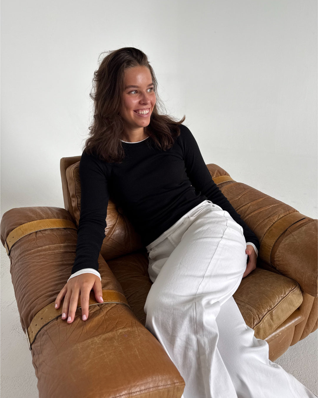 Modelfoto af pige som bærer en langærmet Henna bluse i sort, samt hvide Nanna jeans. Alt fra By Sofie Sønderby