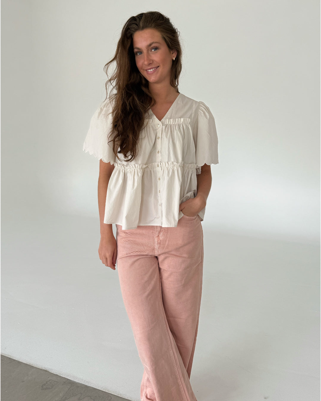 Modelfoto af pige som bærer creme-farvet HOPE top med v-hals og lyserøde jeans. Alt er fra BySofieSønderby