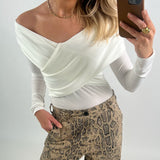 En person med hvid bluse og snakeskin-mønstrede bukser tager et spejlbillede med en smartphone i brun etui. Personen bærer guldsmykker og står i en neutral baggrund.