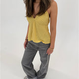 En person står iført en gul top og grå bukser, med hænderne afslappet ved siden, i et lyst, neutralt rum.