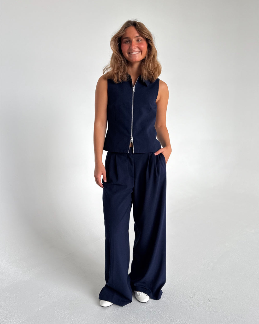 Modelfoto af pige som bærer Kate bukser i Navy, samt Kate top og hvide Alma ballerinaer. Alt fra By Sofie Sønderby
