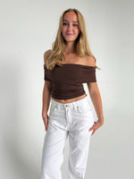 Modelfoto af pige som bærer en Leia top i brun, samt et par hvide Nanna jeans. Alt fra By Sofie Sønderby