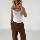 En person tager et spejlfoto med en smartphone. Personen bærer en hvid top og brune bukser i et lyst rum.