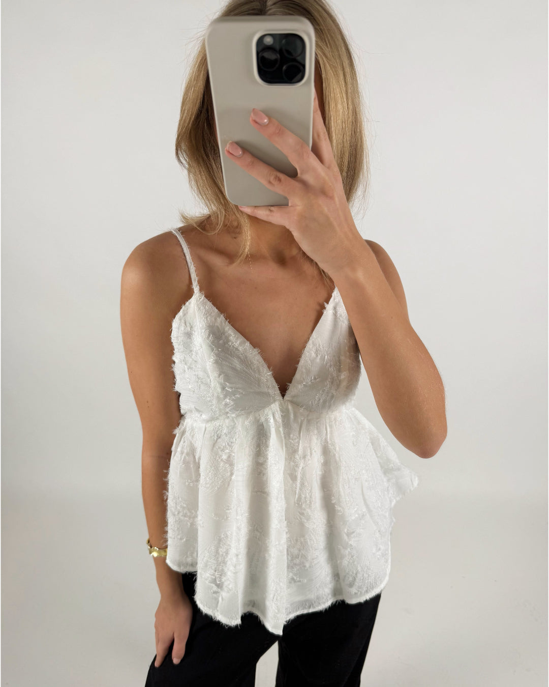 En person iført en hvid top tager et billede med en smartphone foran ansigtet i et lyst rum.