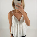 En person iført en hvid top tager et billede med en smartphone foran ansigtet i et lyst rum.