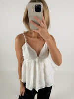 En person iført en hvid top tager et billede med en smartphone foran ansigtet i et lyst rum.