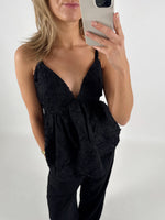 En person iført en sort top med stropper tager et spejlfoto. Personen har lyst hår og står i et lyst rum.