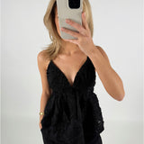 En person iført en sort V-udskåret top tager et spejlbillede med en mobiltelefon, hvor ansigtet er delvist dækket. Baggrunden er enkel og hvid.