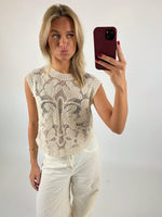 En person tager en selfie med en rød mobiltelefon iført en hvid, mønstret top og hvide bukser. Personen laver en sjov ansigt. Baggrunden er hvid og enkel.