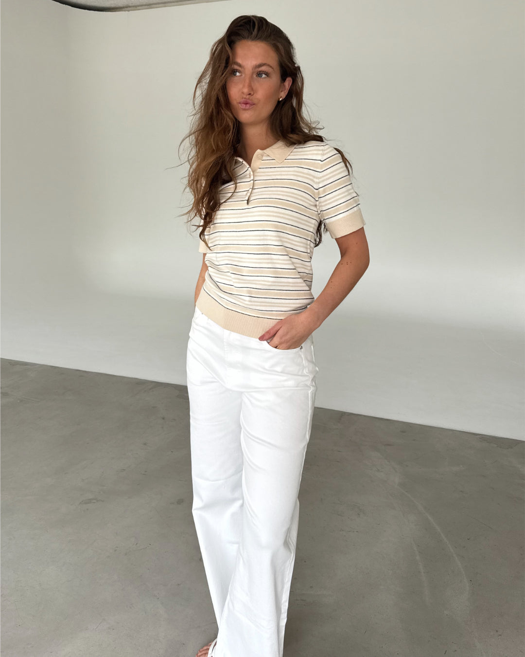 Modelfoto af pige som bærer en LILLIANA beigestribet polo t-shirt og hvide jeans. Alt er fra BySofieSønderby