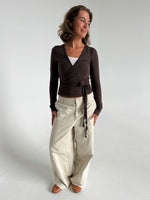 Modelfoto af pige i brun Luna wrapbluse og beige bukser. Fra BySofieSønderby