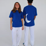 To personer iført blå T-shirts, en vender fremad og en med en halvmåne på ryggen, i et lyst rum iført hvide bukser.