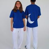 To personer i blå T-shirts og hvide bukser står foran en neutral baggrund; den ene T-shirt har en hvid halvmåne form på ryggen.