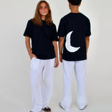 To personer i sorte t-shirts og hvide bukser står sammen; den ene vender mod kameraet, den anden med ryggen til. T-shirten har en stor hvid halvmåne bagpå.