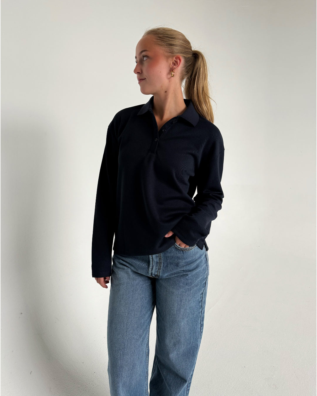 Modelfoto af pige der bærer en navy farvet Millie bluse, samt hvide Nanna jeans. Alt fra BySofieSønderby