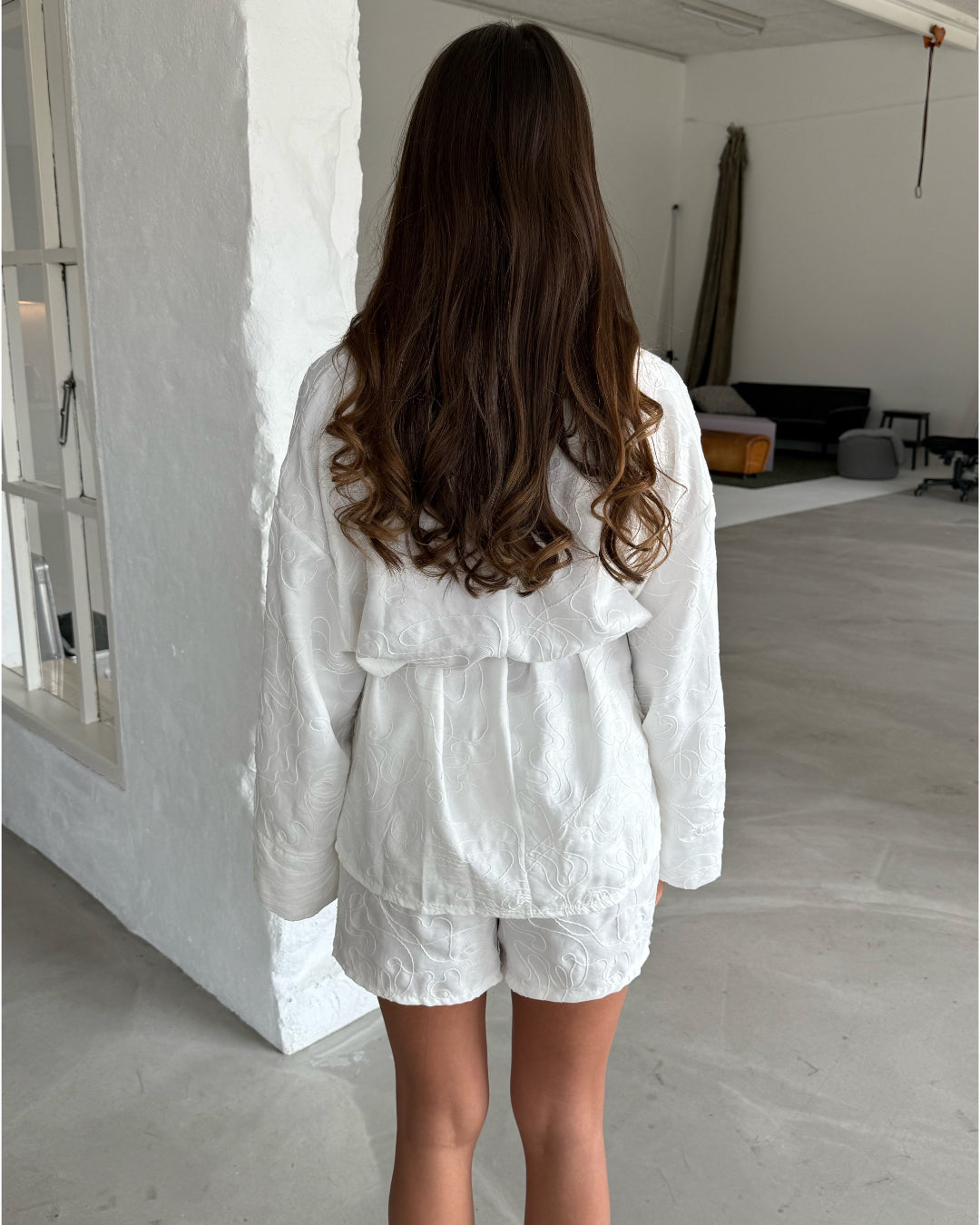 Modelfoto af pige som bærer hvid MIRANDA sæt bestående af slå-om skjorte og shorts med mønster. Set bagfra. Alt er fra BySofieSønderby