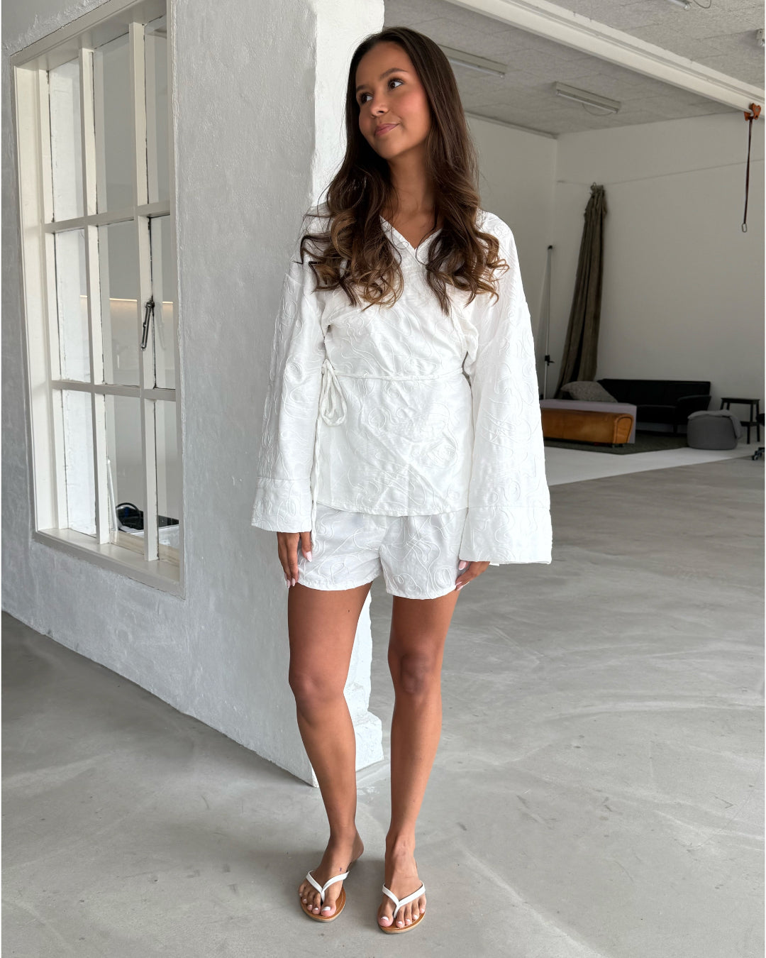 Modelfoto af pige som bærer hvid MIRANDA sæt bestående af slå-om skjorte og shorts med mønster. Alt er fra BySofieSønderby
