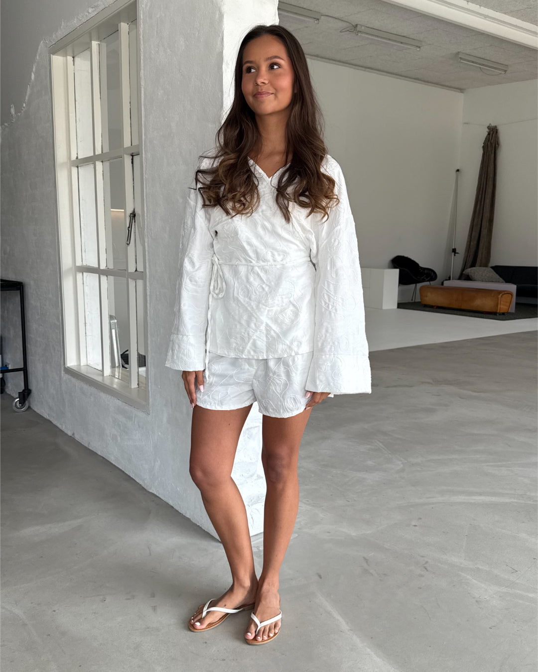 Modelfoto af pige som bærer hvid MIRANDA sæt bestående af slå-om skjorte og shorts med mønster. Alt er fra BySofieSønderby