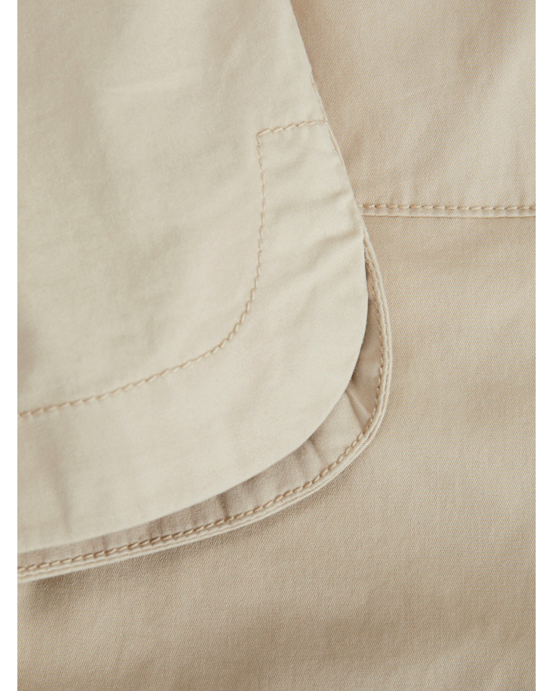 En beige lomme syet på et stykke stof med synlige stikninger. Stoffet har et glat tekstur, og syningerne er jævne. Context er en nærbillede af tekstildetaljer.