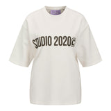 En hvid T-shirt med teksten "STUDIO 2020©" trykt i sort på forsiden. T-shirten hænger frit mod en neutral baggrund.