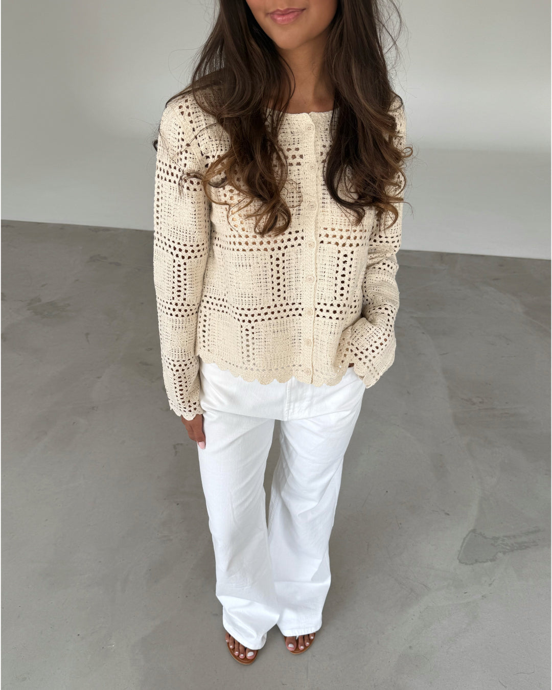 Modelfoto af pige som bærer en cremefarvet ORELLA cardigan med knapper, samt hvide jeans. Alt er fra BySofieSønderby