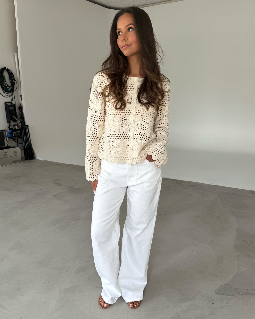 Modelfoto af pige som bærer en cremefarvet ORELLA cardigan med knapper, samt hvide jeans. Alt er fra BySofieSønderby